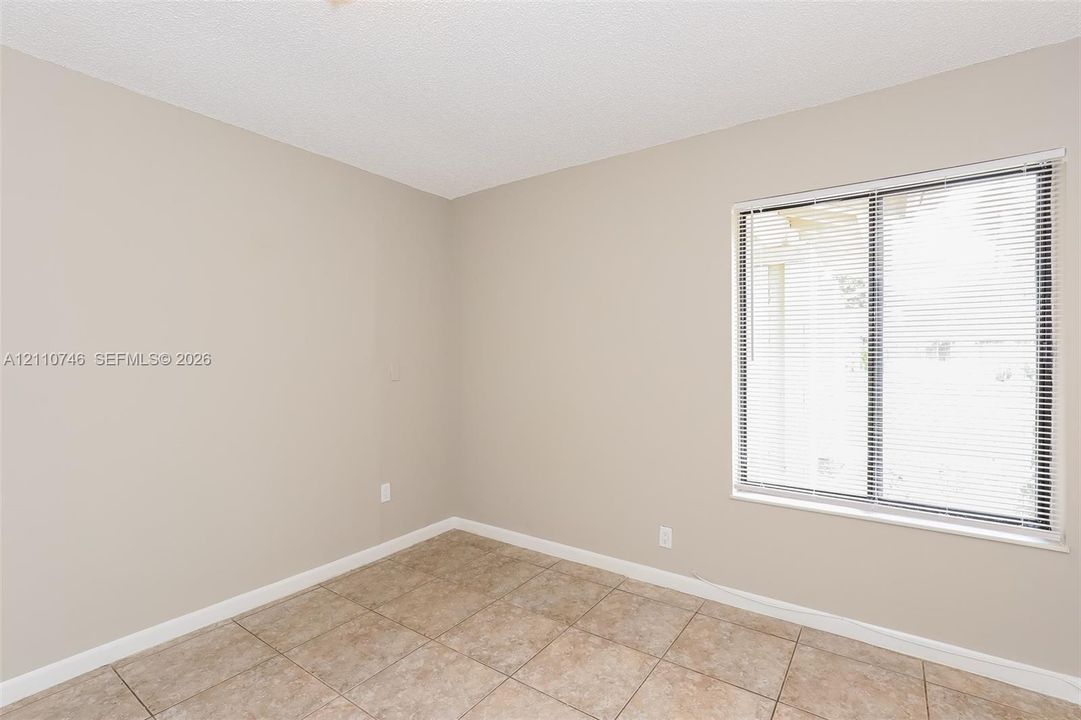 Interior room featuring neutral-toned walls, tile flooring, and a window equipped with horizontal blinds