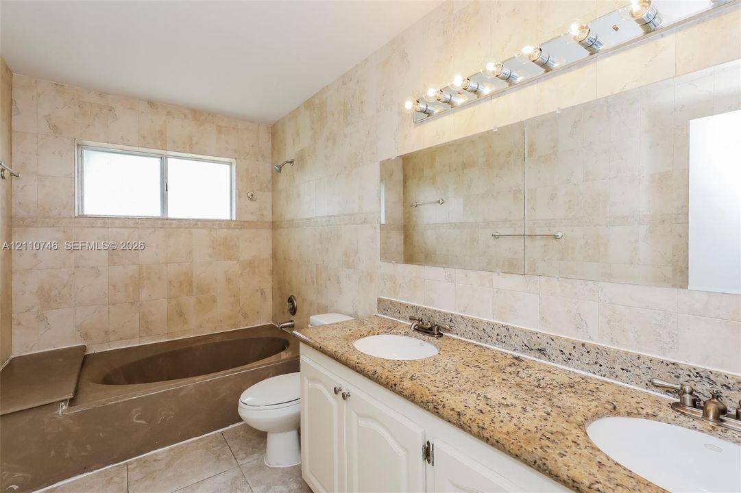 Full-wall tile surround, dual-basin vanity with stone-finish countertop, undermount sinks, and built-in soaking tub