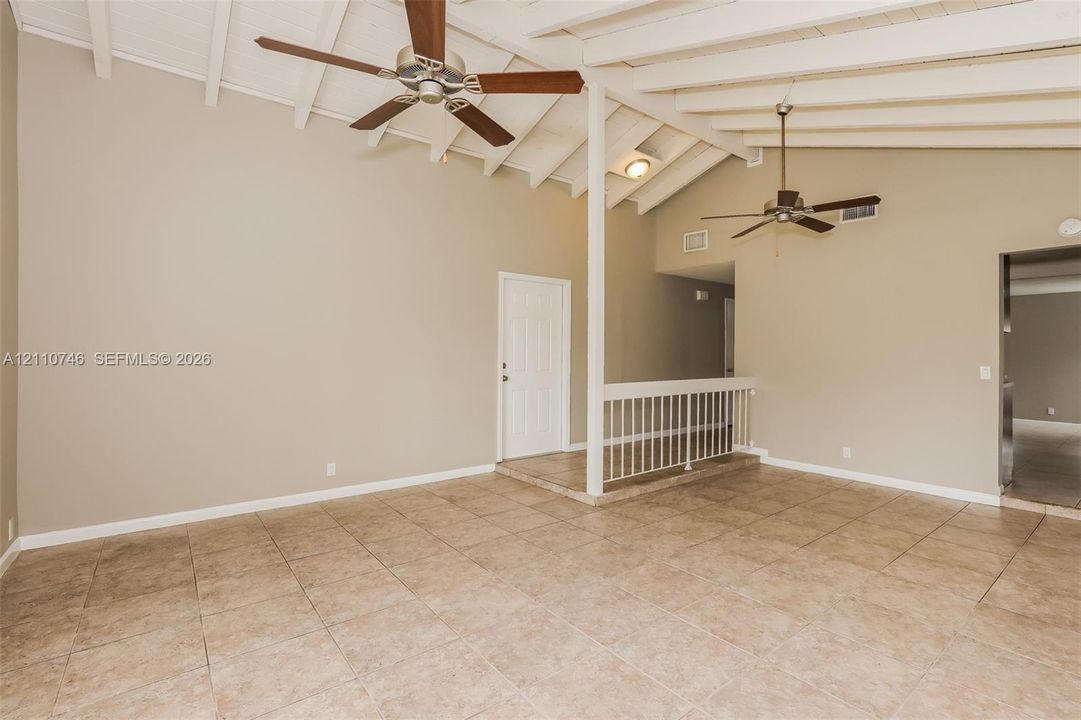 Vaulted ceiling featuring white-painted exposed beams, dual ceiling fans, tile flooring, and a white metal railing