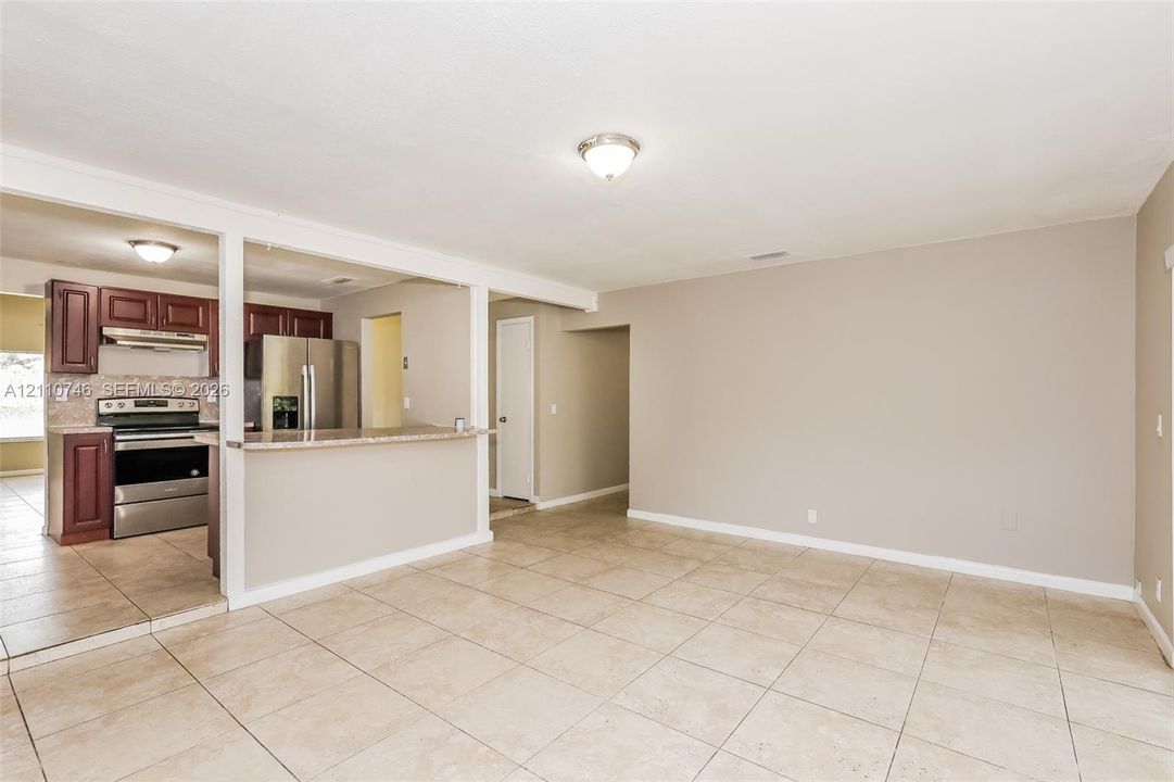 Open-concept space featuring large-format neutral tile flooring and a kitchen peninsula with a stone-finish countertop, dark wood-finish cabinetry, and stainless steel appliances