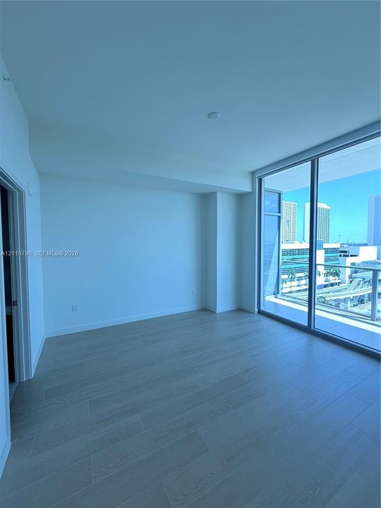Floor-to-ceiling glass sliding doors, wood-finish flooring, and a private balcony with metallic railing