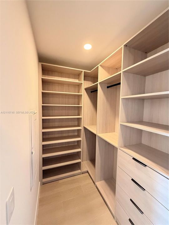 Custom walk-in closet featuring light wood-finish shelving, integrated hanging rods, and a four-drawer built-in storage unit with matte black hardware