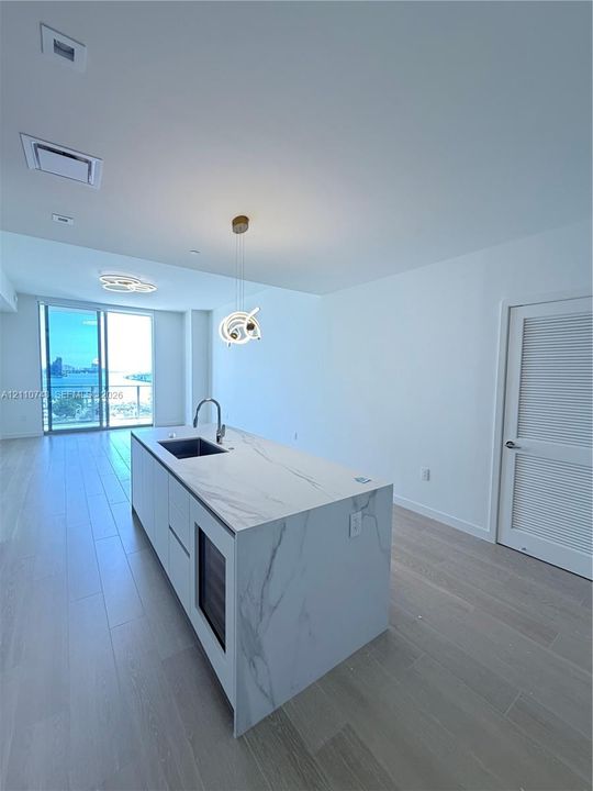 Kitchen island with stone-finish waterfall countertop, undermount sink, built-in wine cooler, and high-arc faucet, complemented by wood-finish flooring and floor-to-ceiling glass panel door