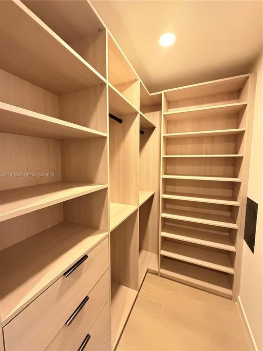 Custom walk-in storage featuring light wood-finish shelving, integrated hanging rods, multi-tier cabinetry, and minimalist matte black hardware