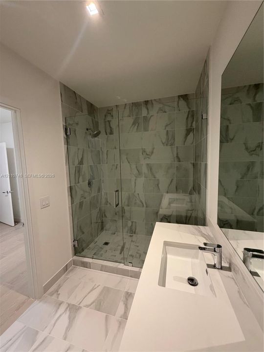 Walk-in shower with floor-to-ceiling tile, frameless glass enclosure, and wall-mounted shower head, paired with a white countertop vanity featuring an integrated rectangular sink and chrome hardware