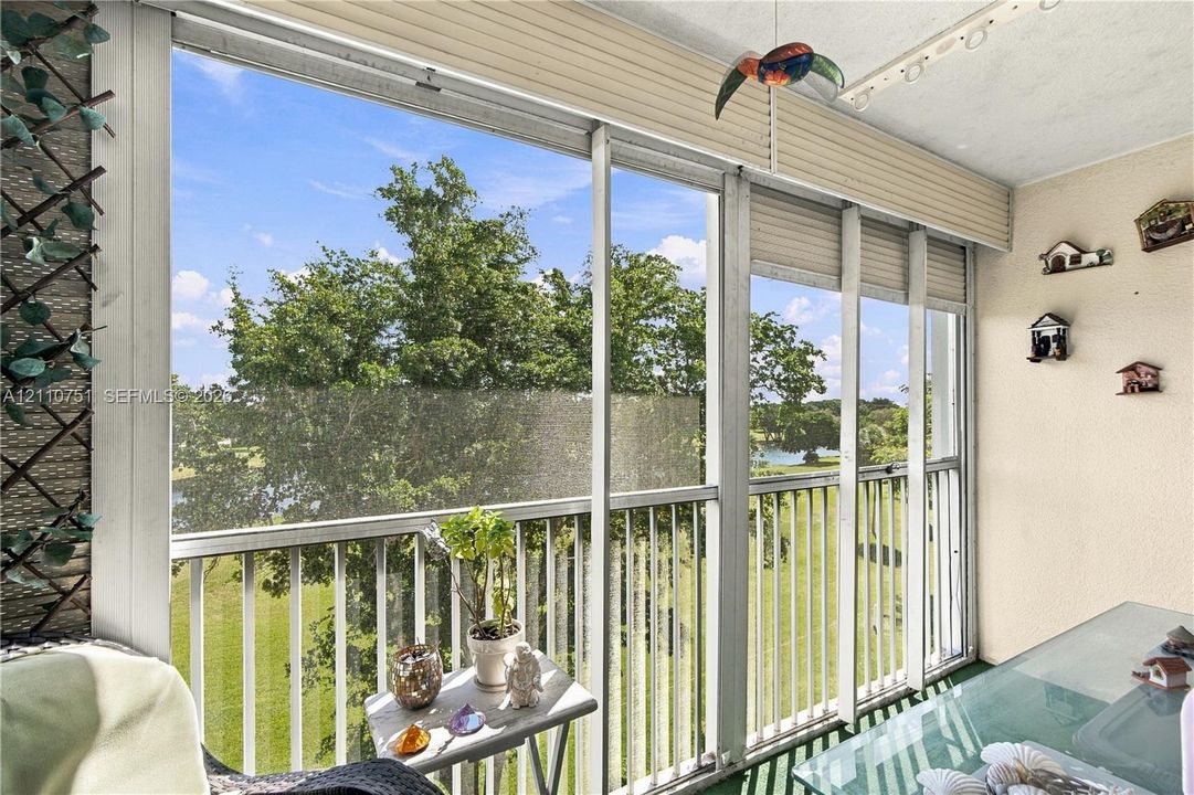 Enclosed porch featuring floor-to-ceiling screened panels, white metal framing, integrated vertical blinds, and green flooring