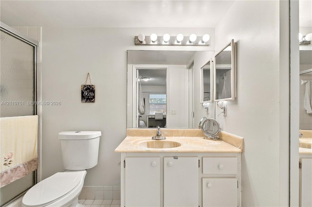 Bathroom featuring a stone-topped vanity with an integrated basin, large-format wall mirror, multi-bulb vanity lighting, and a glass-enclosed shower