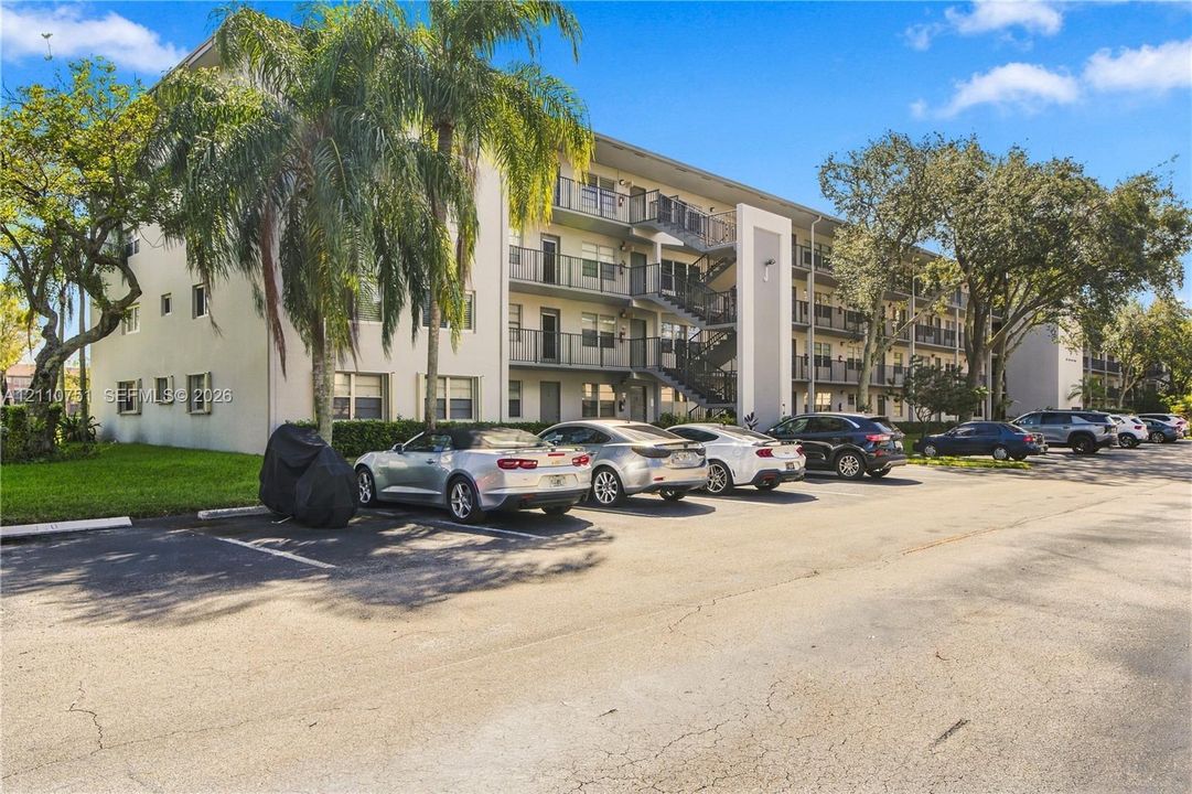 Multi-story exterior building featuring stucco siding, metal balcony railings, external metal staircases, and mature palm trees