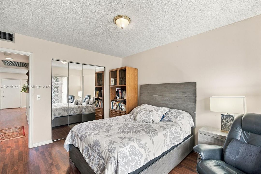 Wood-finish flooring, full-length mirrored sliding closet doors, and a flush-mount dome ceiling light fixture