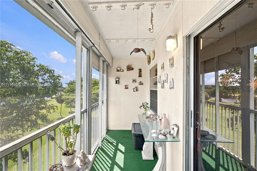 Enclosed balcony featuring floor-to-ceiling screened panels, metal railing, exterior wall sconce, and synthetic turf flooring