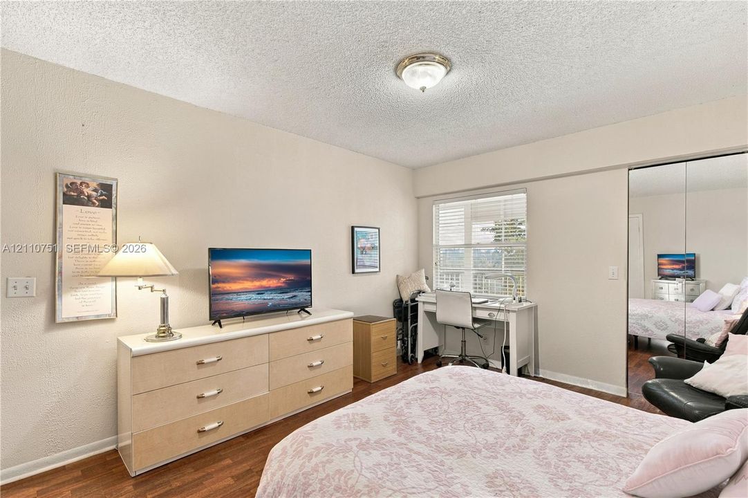 Room with wood-finish flooring, sliding mirror-panel closet doors, and window with horizontal blinds