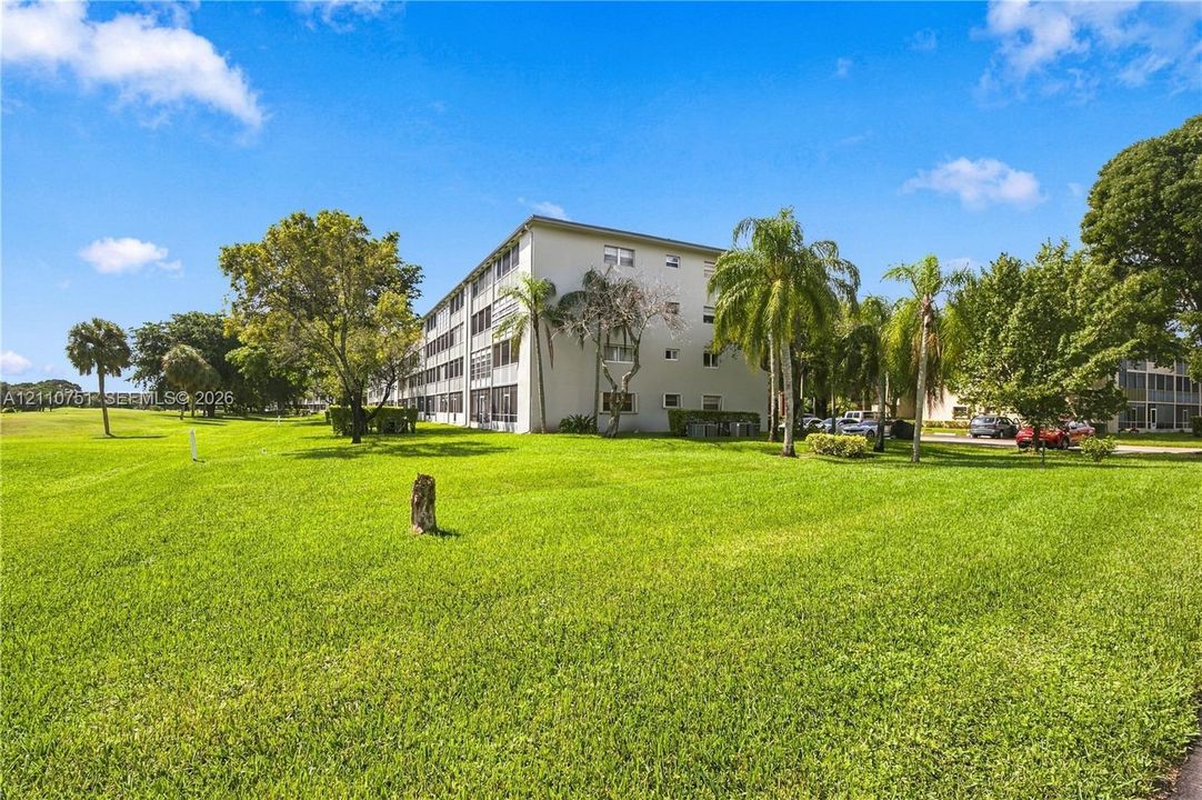 Multi-story residential building featuring a light-toned stucco exterior, expansive lawn, and mature palm trees