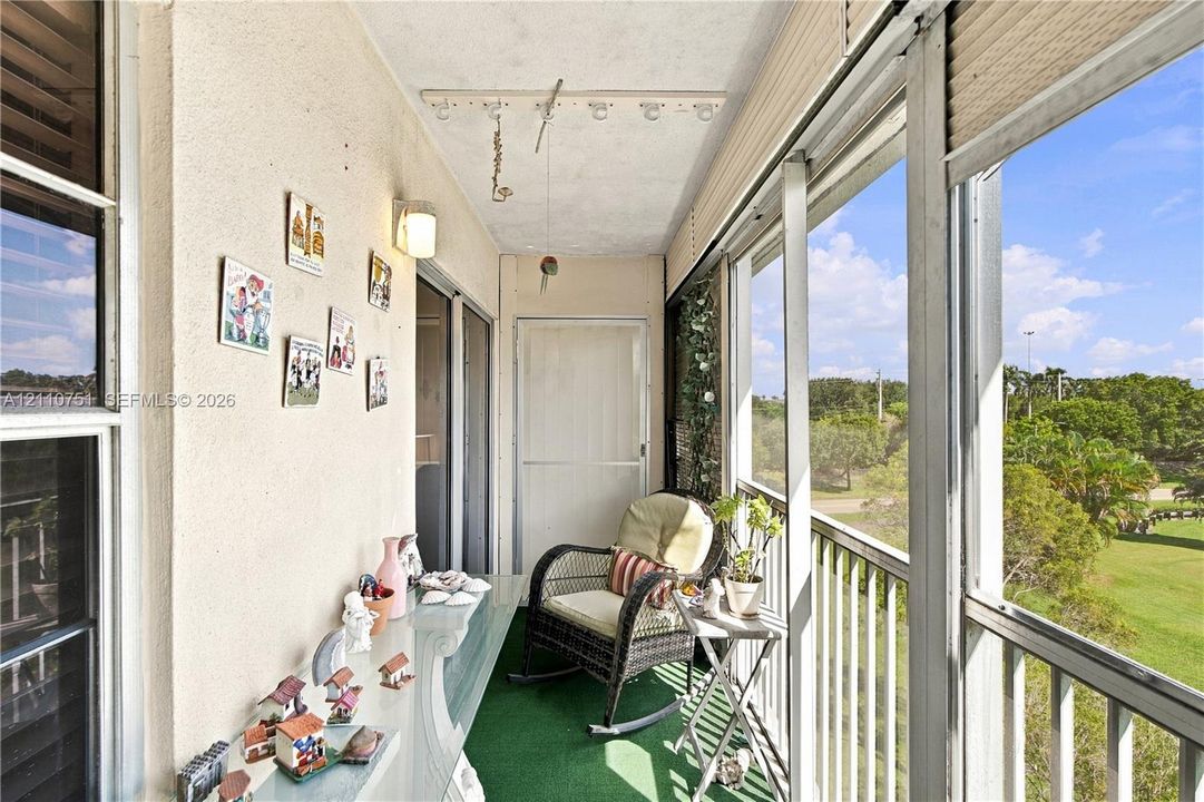 Enclosed balcony featuring floor-to-ceiling glass paneling, metal railing, and wall-mounted lighting