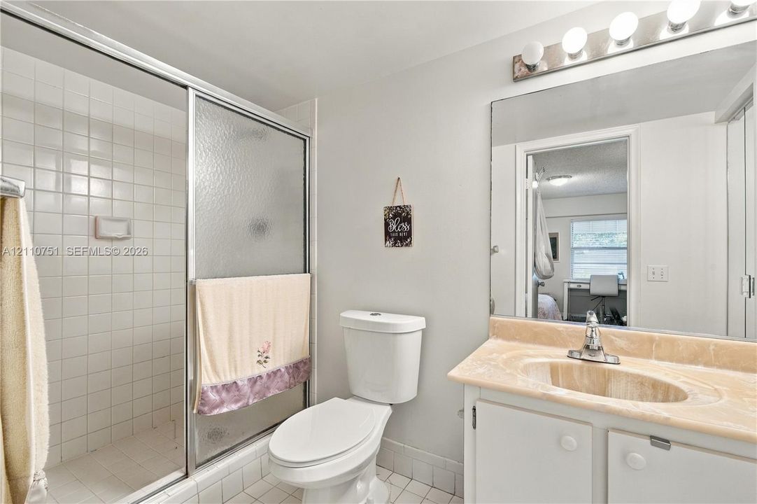 Bathroom featuring a glass-enclosed shower with tiled walls, a vanity with a stone-finish countertop and integrated sink, and a multi-bulb vanity light fixture