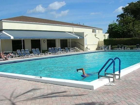 Full-sized swimming pool with white coping, retractable fabric awning, and perimeter paver decking