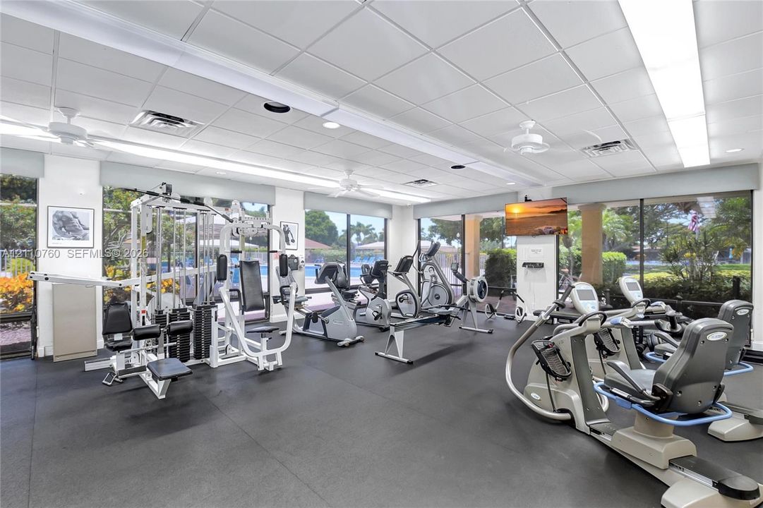 Fitness center featuring drop ceiling tiles, rubberized flooring, ceiling-mounted fans, and floor-to-ceiling windows