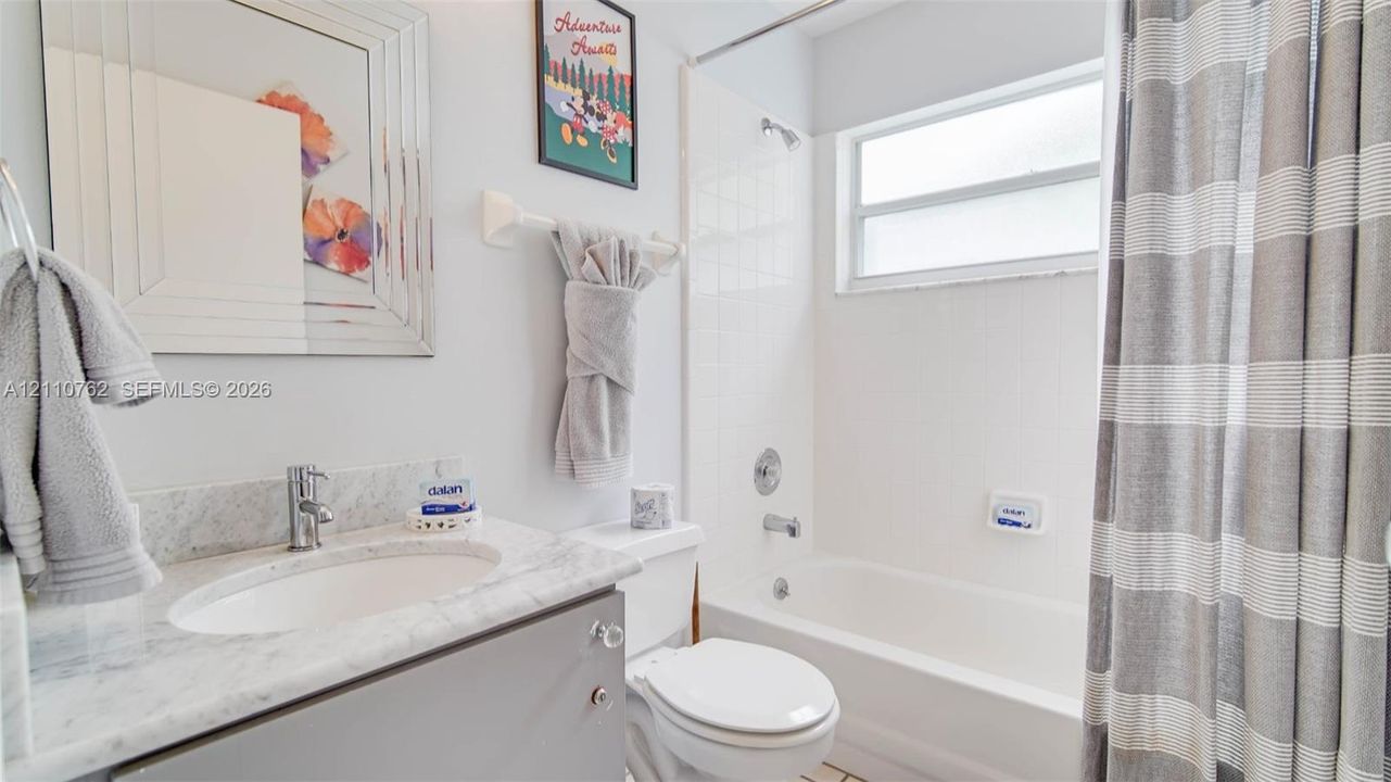 Bathroom featuring a grey vanity cabinet with a stone countertop, undermount sink, chrome faucet, and a tile-surround shower and tub combination
