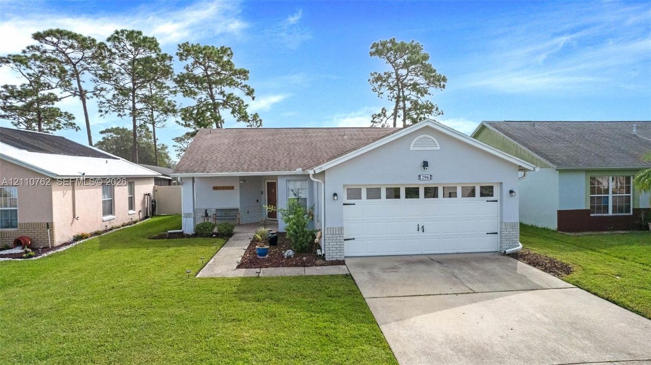 Single-story residence featuring a light-colored stucco exterior, a two-car garage with overhead door, a concrete driveway, a covered front entryway, and a gabled roofline