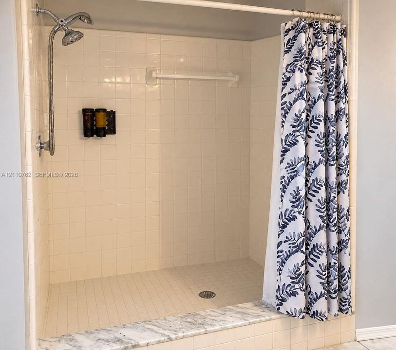 Walk-in shower featuring white wall tiling, a stone-finish threshold, and a wall-mounted metal shower head