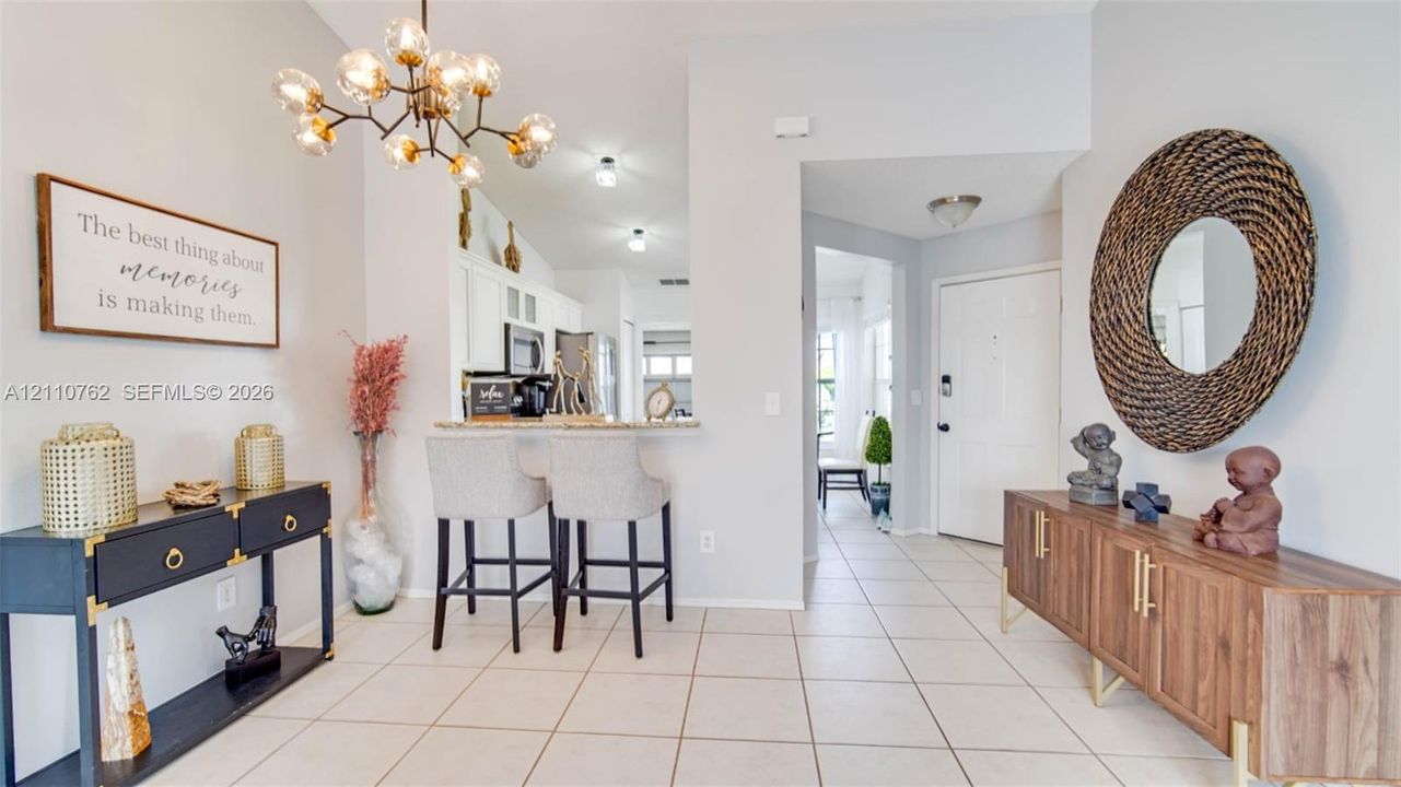 Open-concept interior featuring light tile flooring, a multi-arm modern chandelier, and a built-in breakfast bar with stone-finish countertops