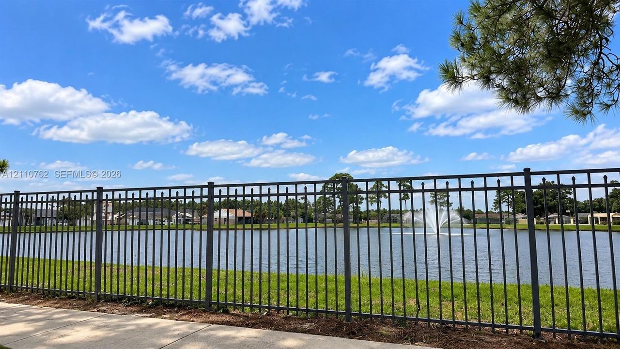 Waterfront lot featuring a metallic picket fence, maintained lawn, and a decorative fountain