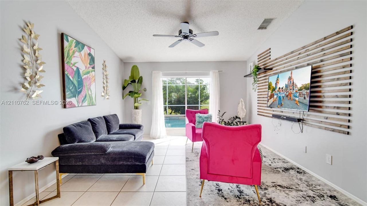 Living area featuring neutral tile flooring, vaulted ceilings with a center fan, and a decorative horizontal wood-slat accent wall