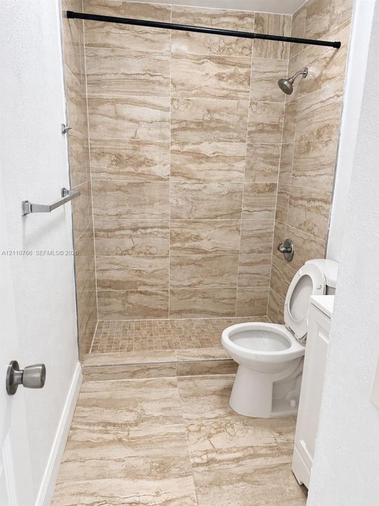Full-height neutral-toned tile shower surround with matching floor tile, walk-in shower stall with mosaic tiled base, and wall-mounted metallic fixtures