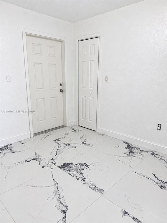 Large-format tile flooring featuring a high-contrast veined pattern, complemented by a six-panel exterior door and matching six-panel closet door