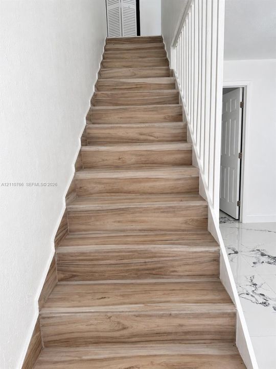 Staircase featuring wood-finish treads and white vertical balusters, complemented by polished tile flooring with marble-style veining