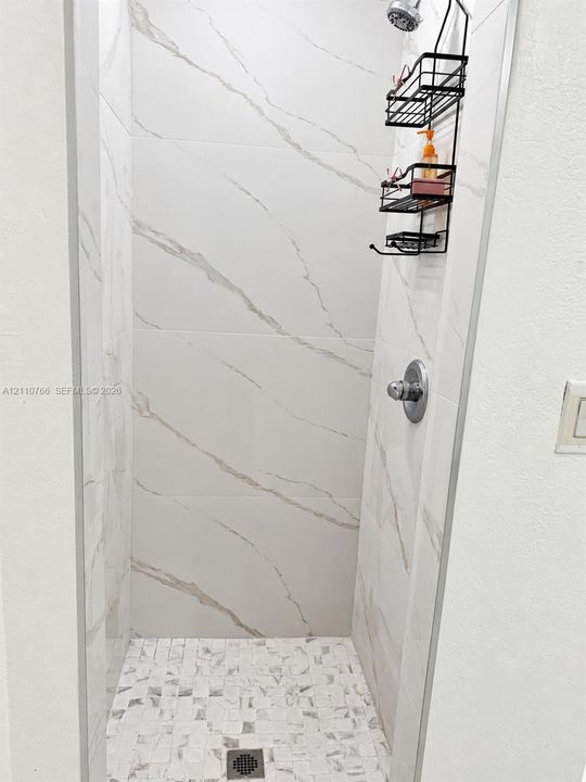 Walk-in shower featuring large-format stone-patterned wall tile, mosaic tile flooring, and a chrome-finish shower valve