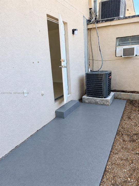 Stucco exterior featuring a dedicated concrete slab, single-step entry, and wall-mounted exterior lighting
