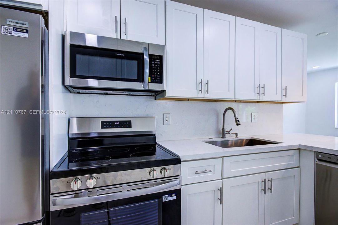 Kitchen featuring white shaker-style cabinetry, stainless steel appliances, white solid-surface countertops, and a single-basin undermount sink with a pull-down faucet