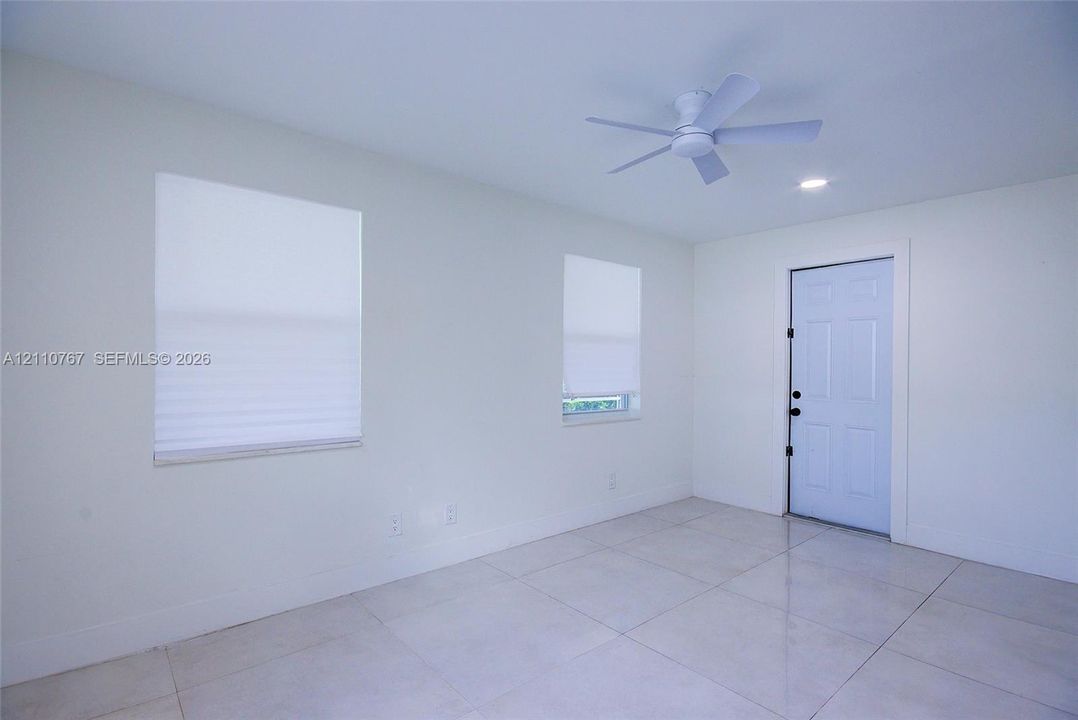Light-filled room featuring neutral tile flooring, a six-panel exterior door, a multi-blade ceiling fan, and recessed lighting