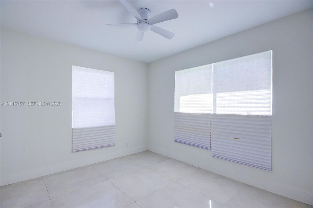 Neutral-toned room featuring large-format tile flooring, a contemporary ceiling fan, and dual windows equipped with cordless pleated shades