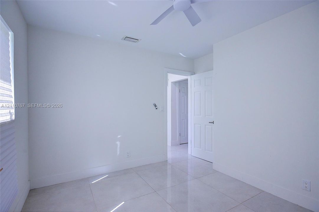 Interior room featuring large-format tile flooring, a neutral white color palette, and a white ceiling fan with integrated lighting