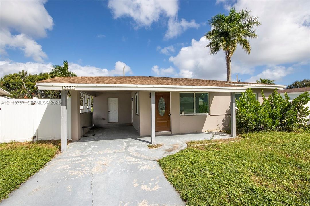 Single-story exterior featuring a covered carport, wood-finish entry door with an oval glass insert, and a white privacy fence