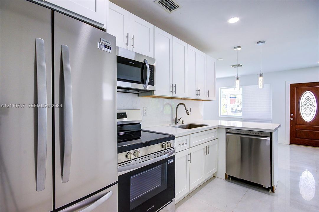 Kitchen featuring white shaker-style cabinetry, stainless steel appliances, solid-surface countertops, dual pendant lighting, and polished floor tile