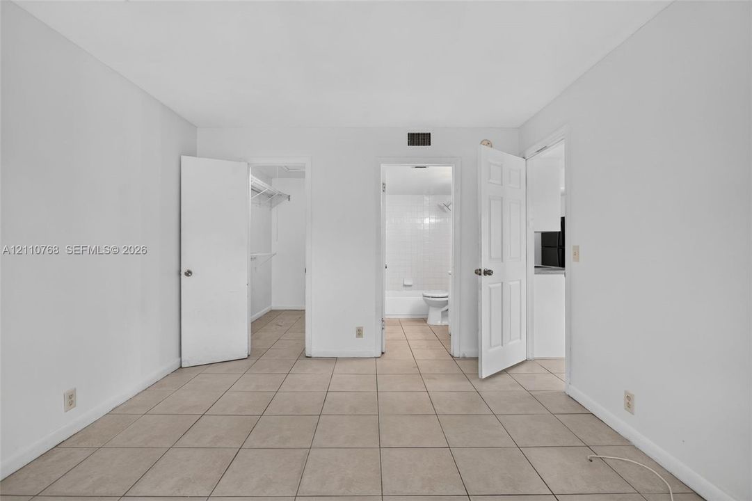 Room interior featuring neutral ceramic tile flooring, two paneled doors, and direct entry points to a walk-in closet and a tiled bathroom