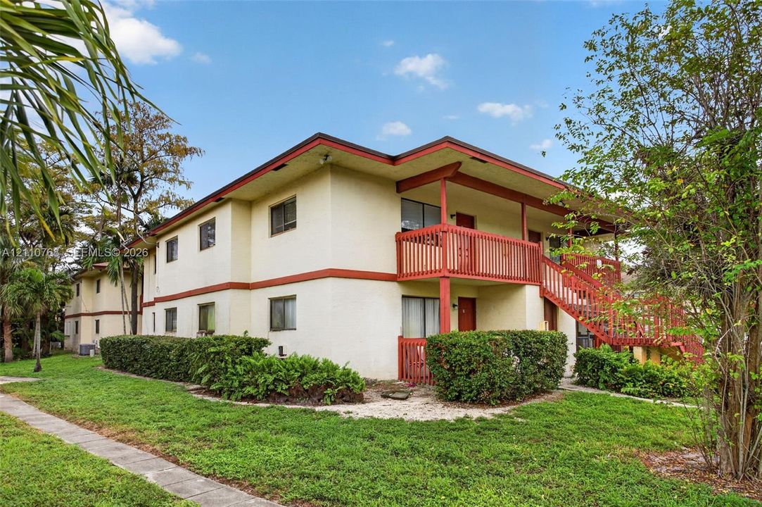 Two-story exterior featuring light-colored stucco siding, contrasting trim, an expansive wood-railing balcony, and a dedicated staircase