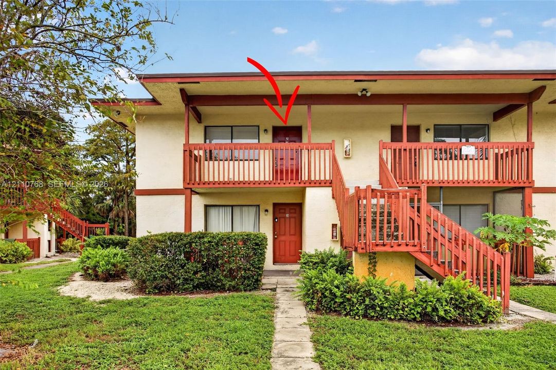 Multi-story exterior featuring a second-level balcony, wood-toned railings, stucco siding, and concrete walkway