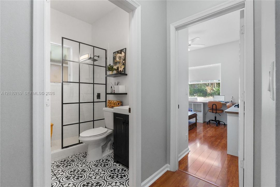 Bathroom featuring a walk-in shower with black-grid glass enclosure, patterned tile flooring, dark cabinetry, and wall-mounted shelving