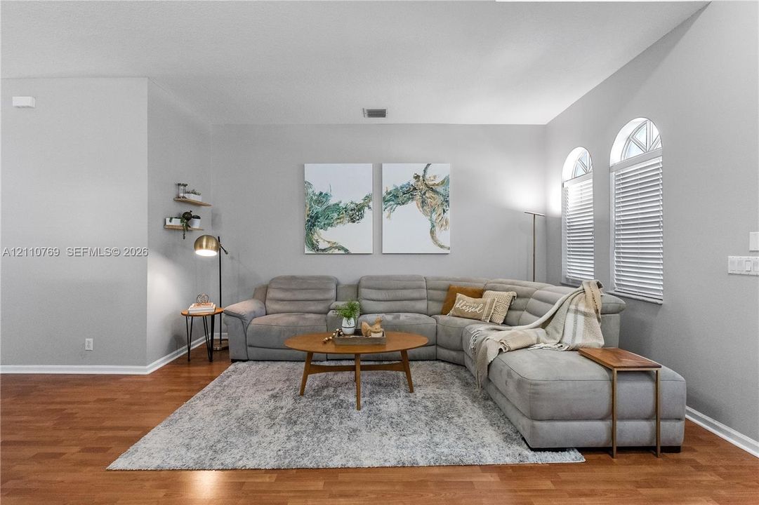 Living area featuring wood-finish flooring, two arched windows, and wall-mounted shelving