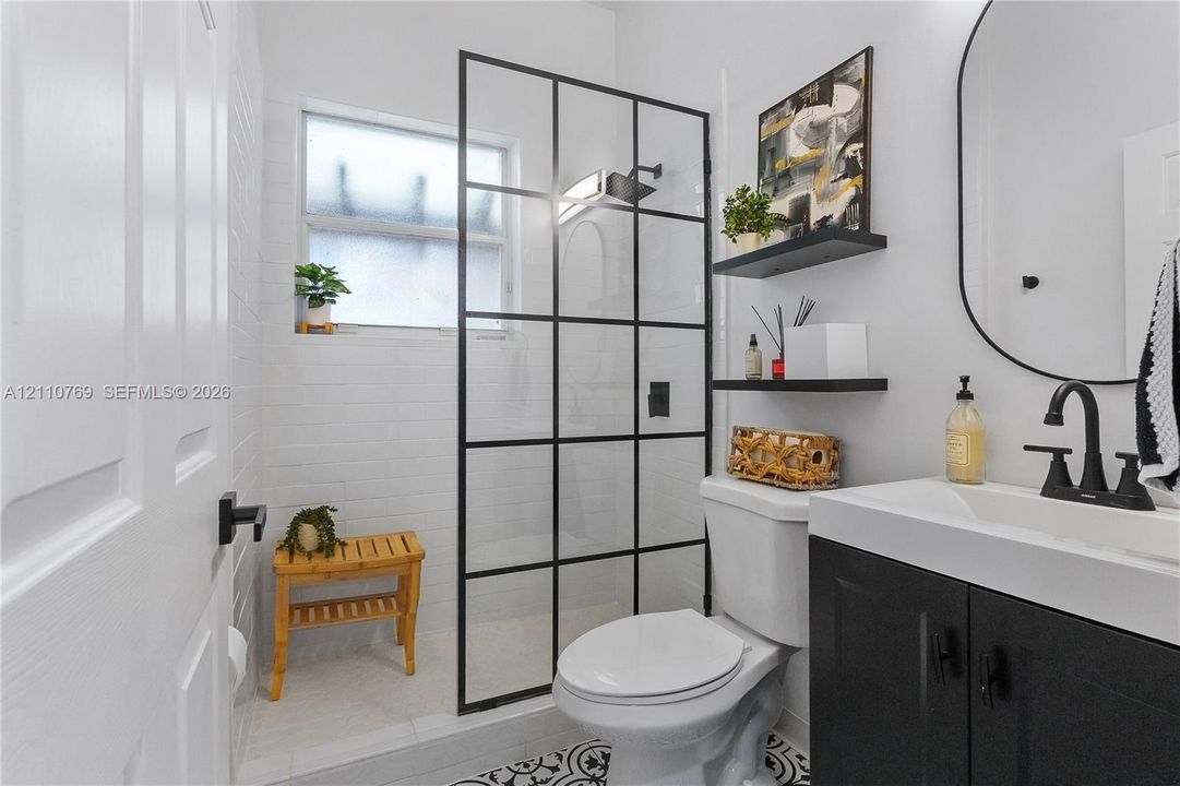 Bathroom featuring a vanity with black cabinetry, a grid-patterned glass shower enclosure, matte black plumbing fixtures, patterned tile flooring, and wall-mounted shelving