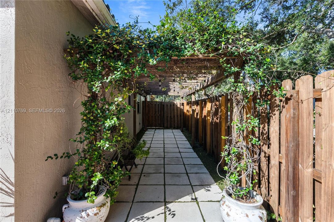 Side walkway featuring square concrete pavers, a wooden pergola, and a privacy fence