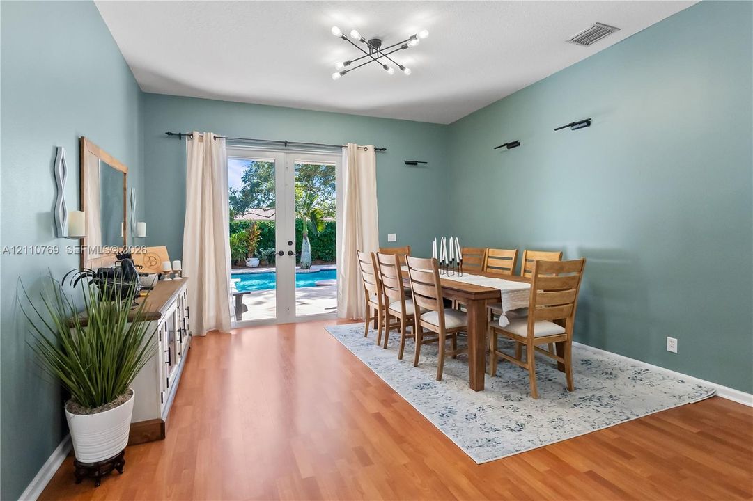 Dining area featuring wood-finish flooring, a multi-arm sputnik chandelier, wall-mounted accent lighting, and French doors leading to an exterior pool