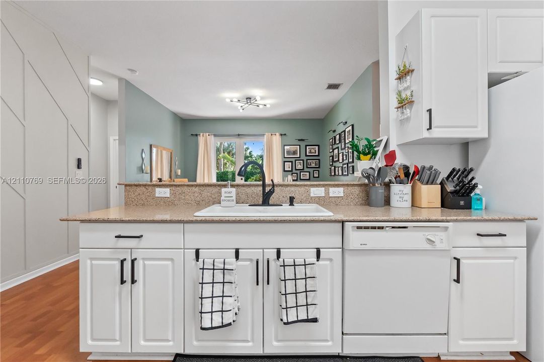 Kitchen featuring white shaker-style cabinetry, neutral stone-finish countertops, undermount sink with matte black faucet, integrated dishwasher, and wood-finish flooring