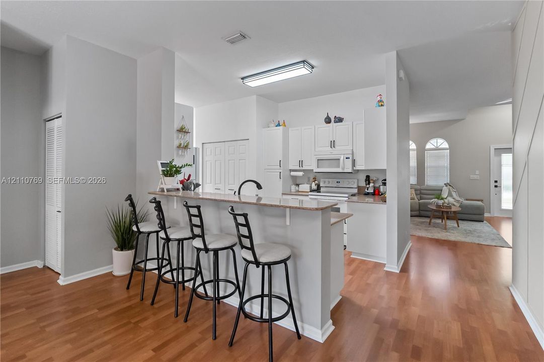Kitchen featuring a tiered breakfast bar, white cabinetry, light-toned stone-finish countertops, and wood-finish flooring