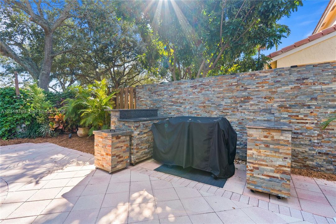 Outdoor kitchen area featuring natural stone veneer cabinetry, dark stone countertops, paver patio flooring, and a stone privacy wall