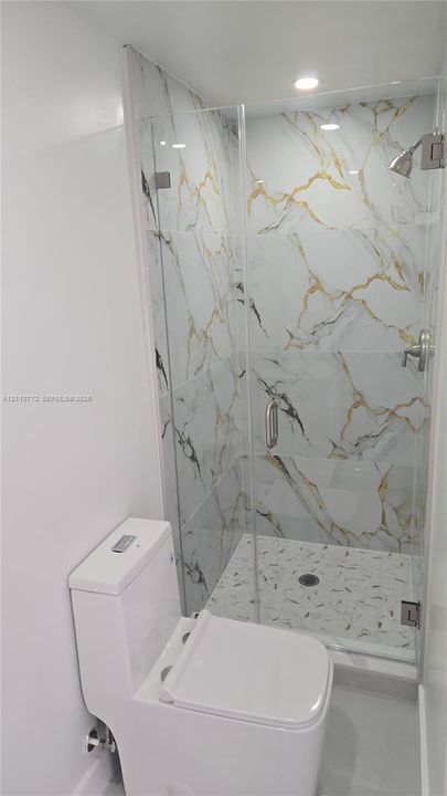 Walk-in shower with floor-to-ceiling veined tile surround, glass enclosure, mosaic-tiled shower floor, and recessed ceiling lighting