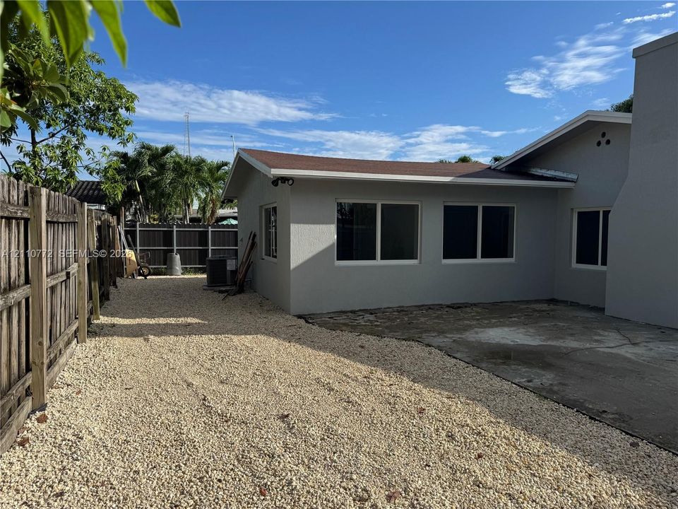 Exterior view featuring a neutral-toned stucco finish, low-maintenance gravel ground cover, and enclosed wooden perimeter fencing